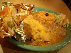 a green plate topped with lots of food on top of a wooden table covered in foil