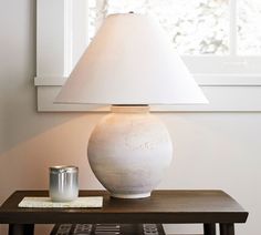 a white lamp sitting on top of a wooden table next to a cup and book