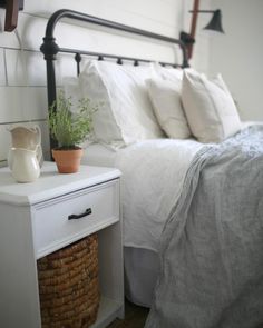 a bed with white sheets and pillows next to a basket filled with plants on top of it