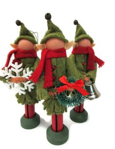 three christmas elves with bells and wreaths on top of each other, standing in front of a white background