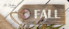 a wooden sign with the word fall written on it next to dried flowers and burlap