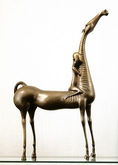 a bronze statue of a giraffe standing on top of a glass shelf next to a white wall