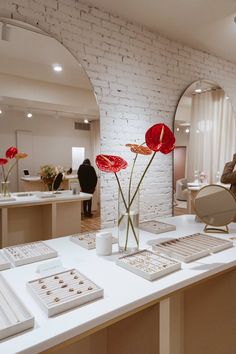 a table with flowers and jewelry on it in front of a mirror that is reflecting the room