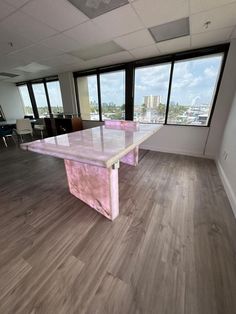 an empty office with large windows and pink table in front of the window is a city view