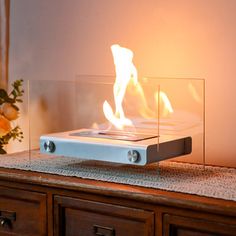 a glass fire place sitting on top of a wooden table next to a vase with flowers