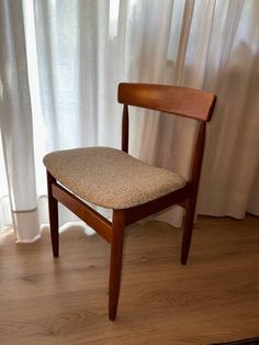 a wooden chair sitting in front of a window next to a white drape curtain