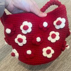 a crocheted red purse with white and red flowers is being held by someone's hand