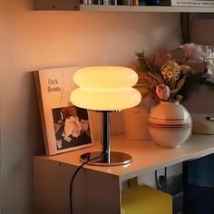 a table with a lamp on top of it next to a book shelf and flowers