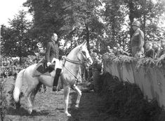 a man riding on the back of a white horse in front of a group of people