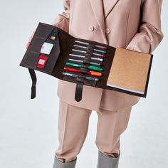 a person in a suit holding a case filled with pens and pencils, including an eraser