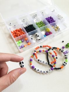 a hand holding a beaded bracelet next to a plastic container filled with beads and skulls