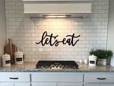 a kitchen with white cabinets and black lettering on the wall above the stove top that says, let's eat