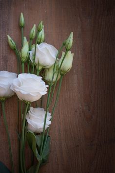 white flowers are arranged on a wooden surface with green stems and leaves in the center