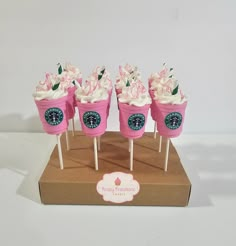 there are cupcakes with white frosting and pink flowers on sticks in the box