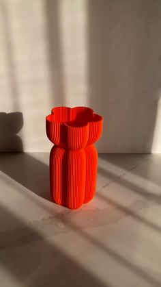 an orange vase sitting on top of a white counter next to a shadow cast wall