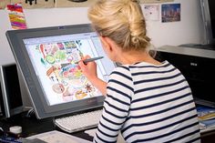 a woman sitting at a desk drawing on a computer screen