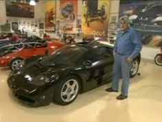 a man standing next to a black sports car in a showroom filled with other cars