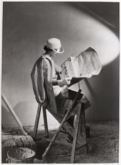 a woman sitting in a chair reading a book while holding a shovel and wearing a hat