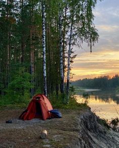 a tent is set up on the edge of a cliff near a lake at sunset