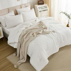 a bed with white comforters and pillows in a room next to a window filled with curtains