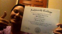 a woman holding up a certificate in front of her face and giving the thumbs up