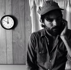 a man sitting in front of a clock talking on a cell phone