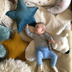 a baby laying on top of a bed next to some pillows and stuffed animal toys