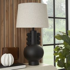 a table lamp sitting on top of a white table next to a book and potted plant