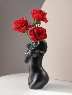 there is a black vase with three red roses in it on a white countertop