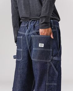 The Recycled Cotton Denim Wide Pants are heavy-weight denim utility pants. The pants feature slanted pockets at the waist, open-top pockets on the back, tool pockets and loops at the thigh on both sides, elastic shirring at the waist, and belt loops. The material is a 12.6oz recycled denim with reinforced stitching. Dark Wash Utility Cargo Jeans With Belt Loops, Utility Jeans With Hip Pockets In Rigid Denim, Dark Wash Rigid Denim Jeans, Utility Rigid Denim Cargo Jeans With Five Pockets, Utility Dark Wash Jeans With Patch Pockets, Utility Style Dark Wash Jeans With Patch Pockets, Urban Style Rigid Denim Jeans With Pockets, Dark Wash Utility Jeans With Patch Pockets, Urban Rigid Denim Jeans With Pockets