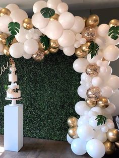 a white and gold wedding cake surrounded by large balloons in front of a green wall