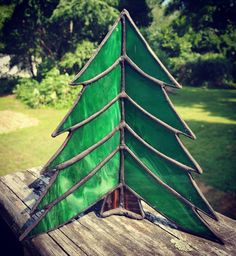 a green glass christmas tree sitting on top of a wooden table in front of trees