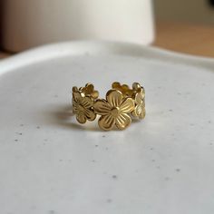 a gold ring with four leaves on it sitting on top of a white table next to a cup