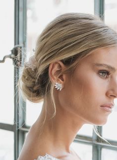 a woman in a white dress is looking out the window with her hair pulled back