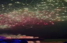 fireworks are lit up in the night sky with people looking on from the water below