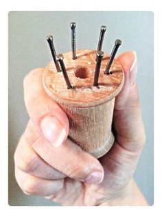 a hand holding a small wooden object with nails in it's center and four screws sticking out of the top