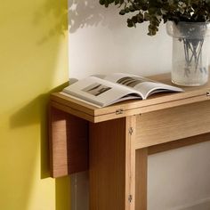 an open book on a wooden table next to a vase with green plants in it