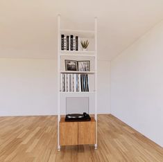 there is a book shelf with books and records on it in the middle of an empty room