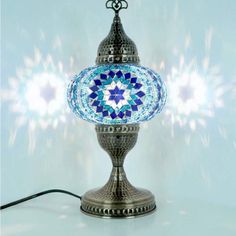 a blue and white mosaic glass lamp on a silver stand with a black cord plugged into it