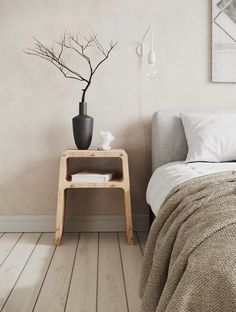 a bed room with a neatly made bed and a plant on the end table next to it