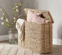 a basket sitting on the floor next to a vase with flowers in it and a throw pillow