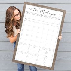 a woman holding up a large framed calendar on the side of a house with her hands