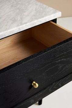 an open drawer with marble top sits on a white countertop next to a black cabinet