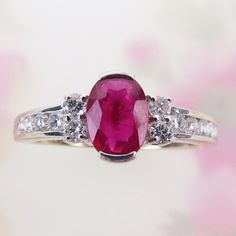 A vibrant natural ruby is centered on this attractive 14k white gold diamond ring. The .65 carat ruby is of deep raspberry pinkish-red color. It measures 6.5mm x 5mm x 2.5mm and is tightly held by two half-bezels.  Four bright and sparkly 2mm .03 carat diamonds flank the red gem. The shoulders are channel set with four 1.5mm diamonds (eight qty. with .12 carat total weight). Collectively, the ring has an estimated total weight of .25 carat or 1/4 carat. The inside is signed, "STS" (STS Jewelry Co., based in Austin, TX) and hallmarked "14k" (white gold). Please see detailed measurements below. The ring is in beautiful condition and would be lovely as an engagement ring or everyday statement ring. Wt: 2.5 grams US Ring size : 6.75 Length: 7.5mm or just over 1/4 Inch Width: 20mm or 13/16 Inch Oval Ruby Ring With Diamond Accents For Promise, Oval Diamond Ring With Lab-created Ruby Accents, Red Oval Sapphire Ring With Brilliant Cut, Red Oval Diamond Ring With Accents, Lab-created Ruby Ring With Brilliant Cut In Oval Shape, Oval Red Diamond Ring With Accents, Red Oval Solitaire Diamond Ring, Oval Lab-created Ruby Diamond Ring In White Gold, Oval Lab-created Ruby Diamond Promise Ring