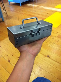 a hand holding a metal briefcase on top of a hard wood floored flooring