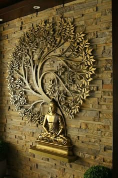 a buddha statue sitting in front of a stone wall with a tree on it's side