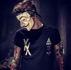 a man wearing a mask with tattoos and piercings on his arm is standing in front of a mirror