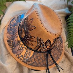 a brown hat sitting on top of a table next to green leaves and plants in the background