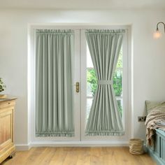 a bedroom with wooden floors and green curtains on the windowsills, next to a bed