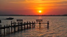 the sun is setting over the water and there are benches on the end of the pier